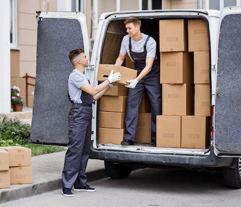 Two young handsome movers wearing uniforms are unloading the van full of boxes. House move, mover service.
